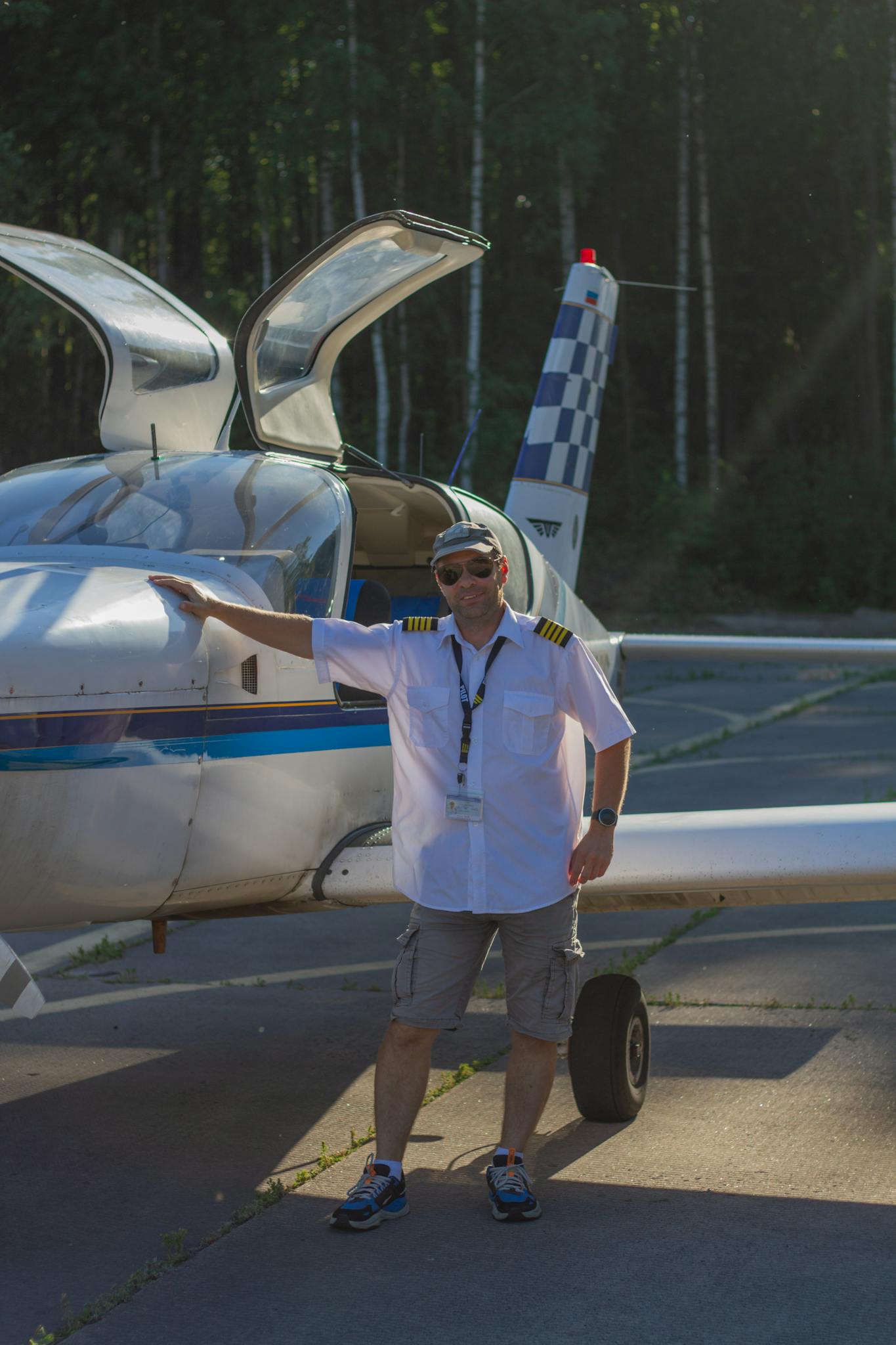 Pilot in uniform stands confidently beside a small aircraft on a sunny day.