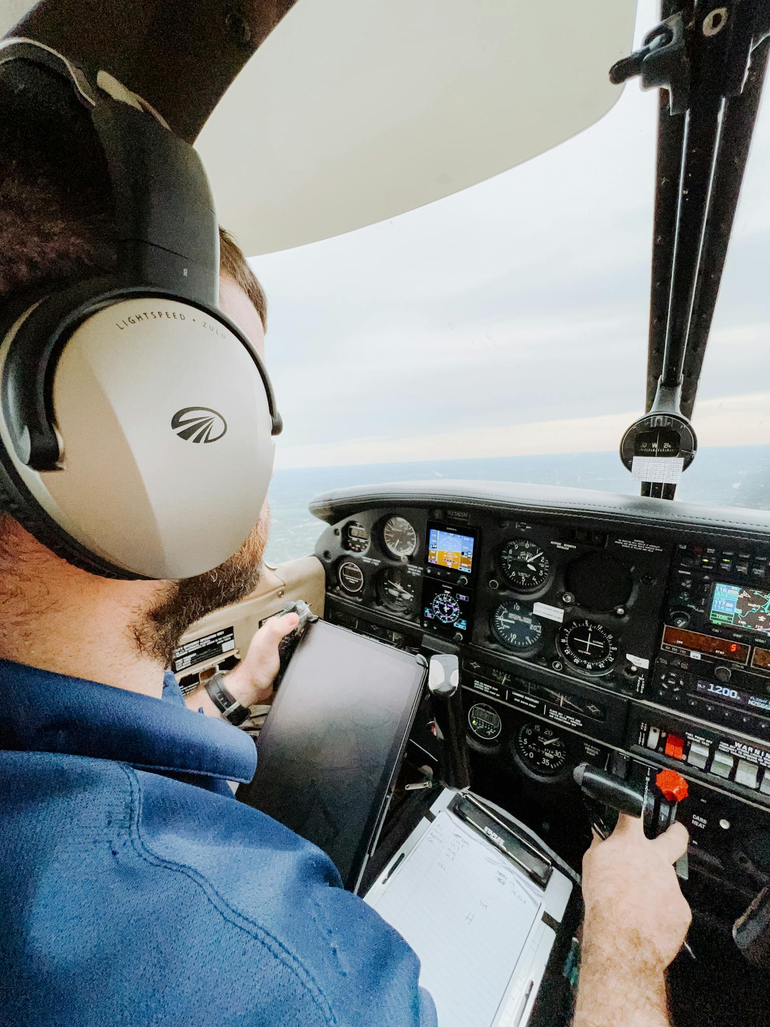 Pilot operating a small aircraft from the cockpit, wearing headphones and navigating at sunset.